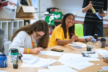 Students painting and drawing together in an art classroom during summer camp.